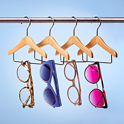 Sunglasses hanging on wooden hangers; styles include tortoiseshell, blue, beige, and pink with mirrored lenses.