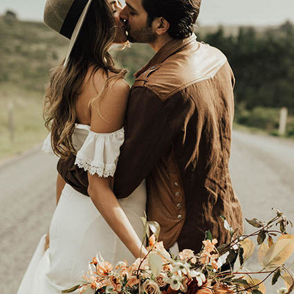 Close-up of a couple kissing, featuring a woman holding a bouquet of peach and white flowers.