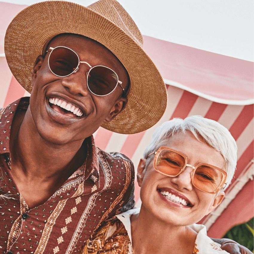 Two smiling individuals wearing stylish sunglasses; one in a straw hat.