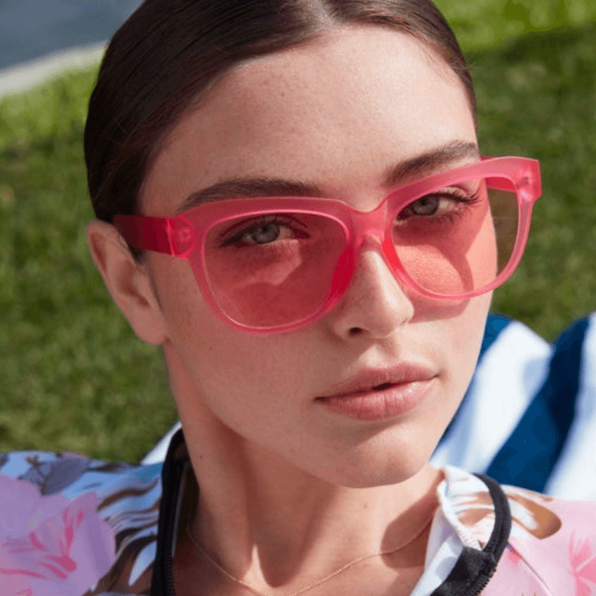 Woman wearing pink transparent sunglasses with pink lenses.