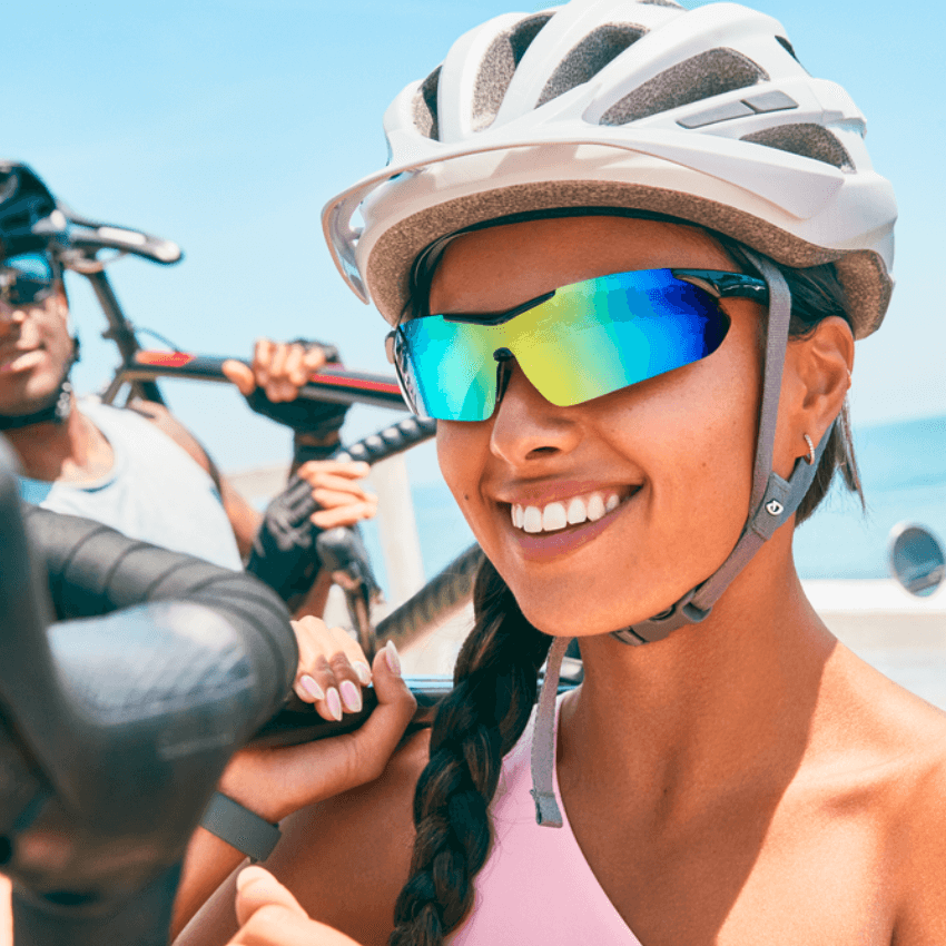 Woman wearing reflective cycling sunglasses and a white helmet, smiling while holding a bicycle.