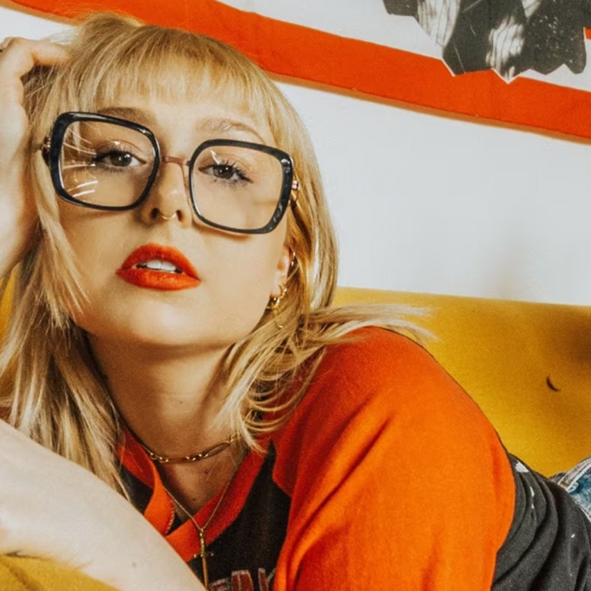 Woman wearing oversized square glasses with black frames, red lipstick, and a red and black shirt.