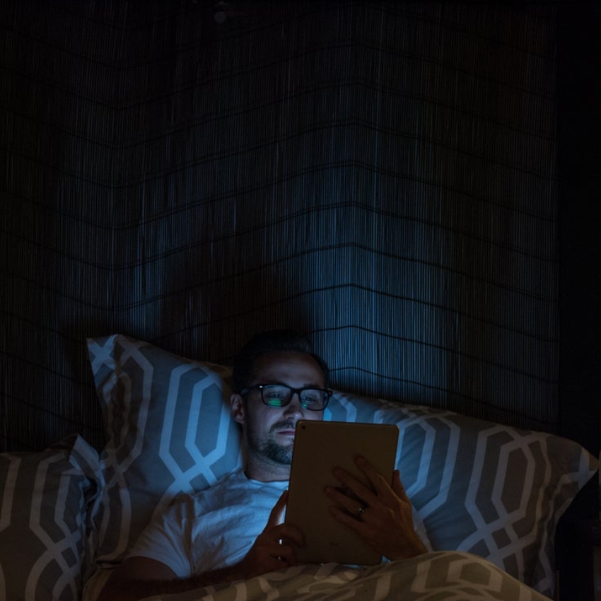 Man wearing glasses using a tablet in bed at night.