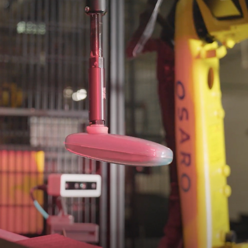 Robotic arm from OSARO holding a red disc-shaped object.