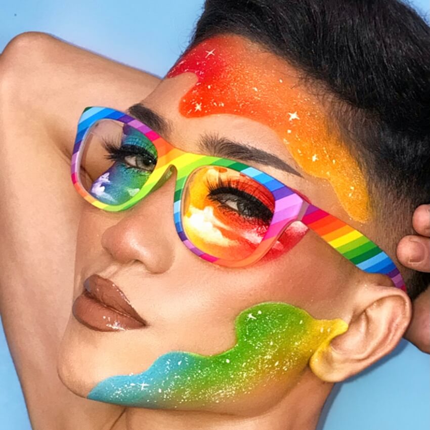 Rainbow-colored glasses with mirrored lenses reflecting a vibrant sky, worn with matching rainbow makeup.