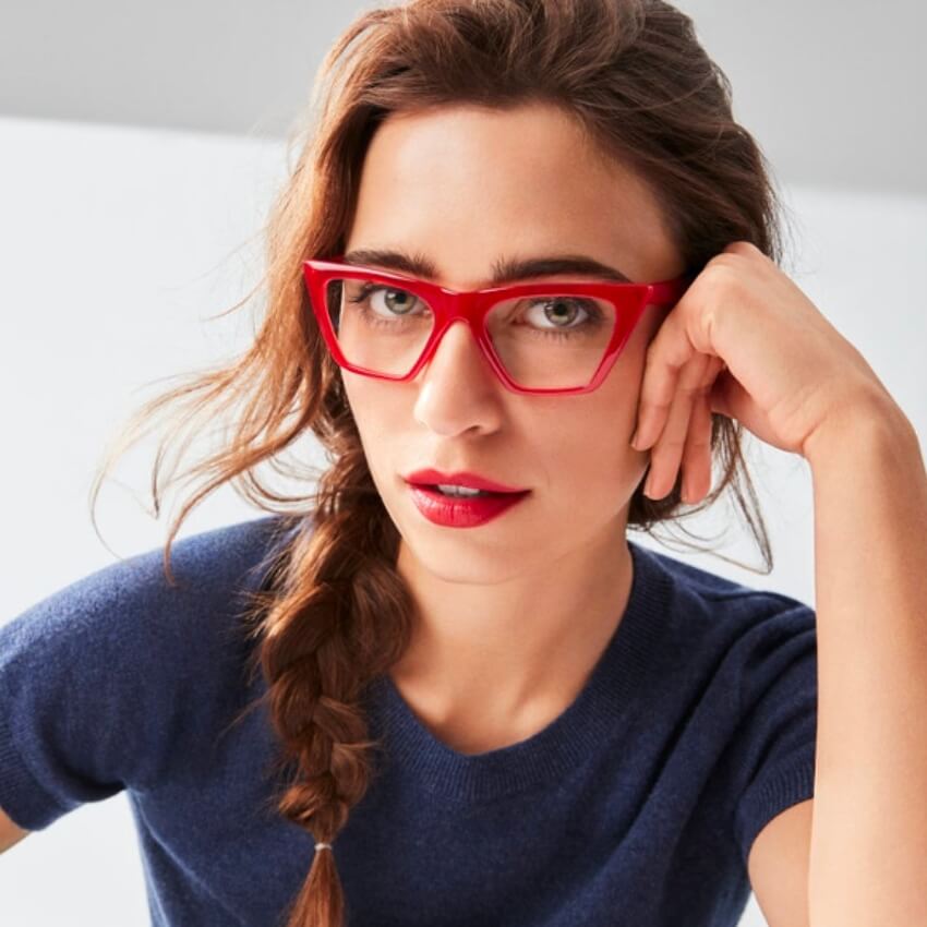 Woman in red-framed glasses and blue sweater, with hair in a side braid.