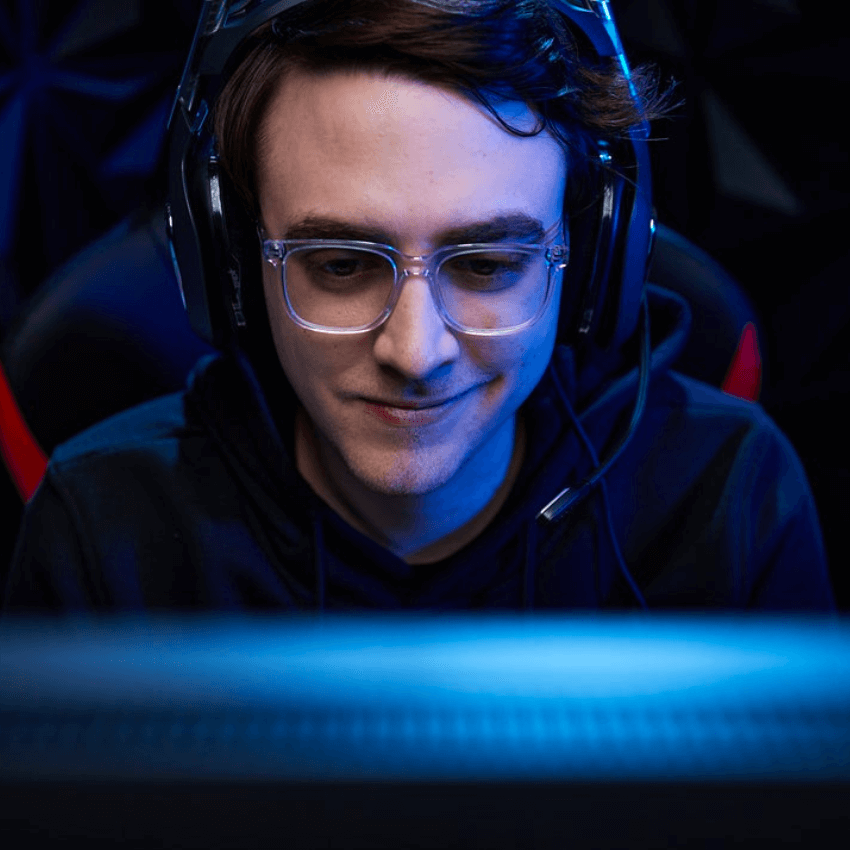 Man wearing large headphones and glasses, smiling while looking at a screen with a blue glow.