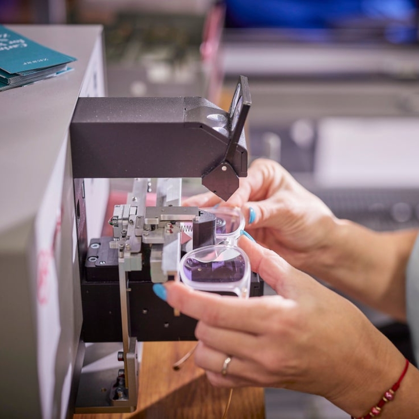 Person adjusting eyeglasses using a lens-cutting machine.