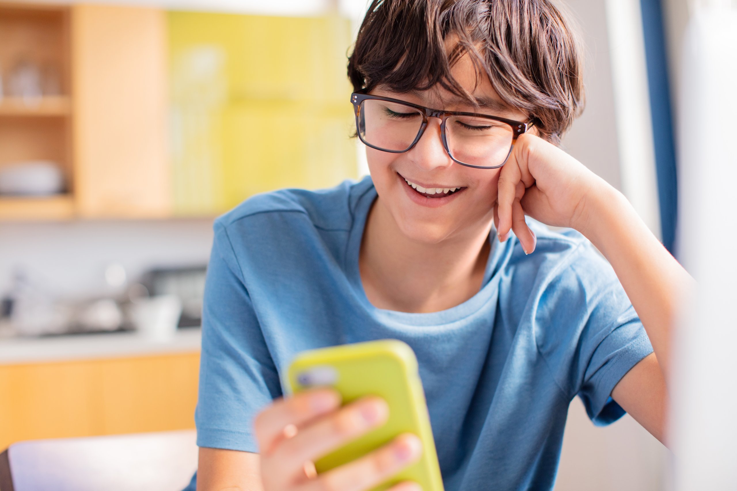 Young person in a blue shirt and glasses smiling at a yellow phone.