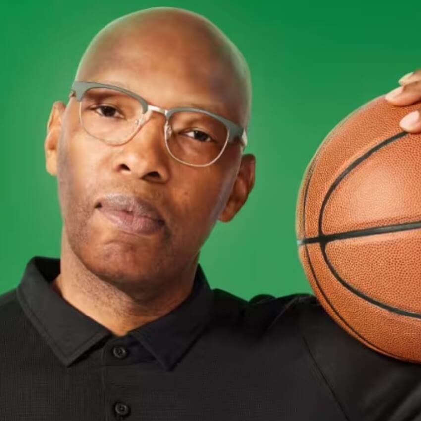 Bald man with glasses holding a basketball against a green background.