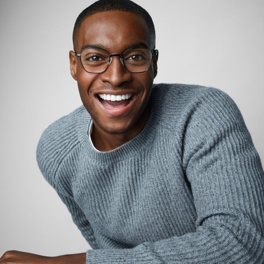 Person wearing a grey ribbed sweater and glasses, smiling broadly.