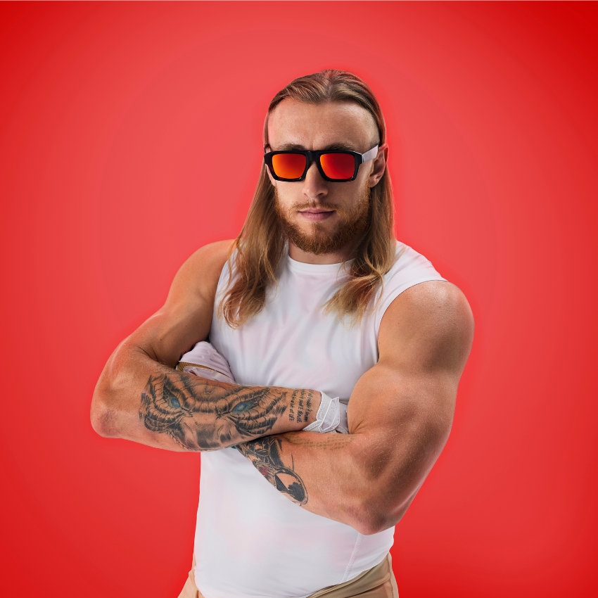 Man wearing mirrored sunglasses, white compression tank top, showcasing arm tattoos.