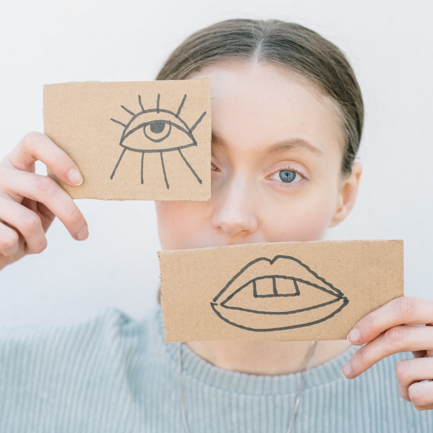 Cardboard pieces drawn with an eye and mouth held by a person covering their real eye and mouth.