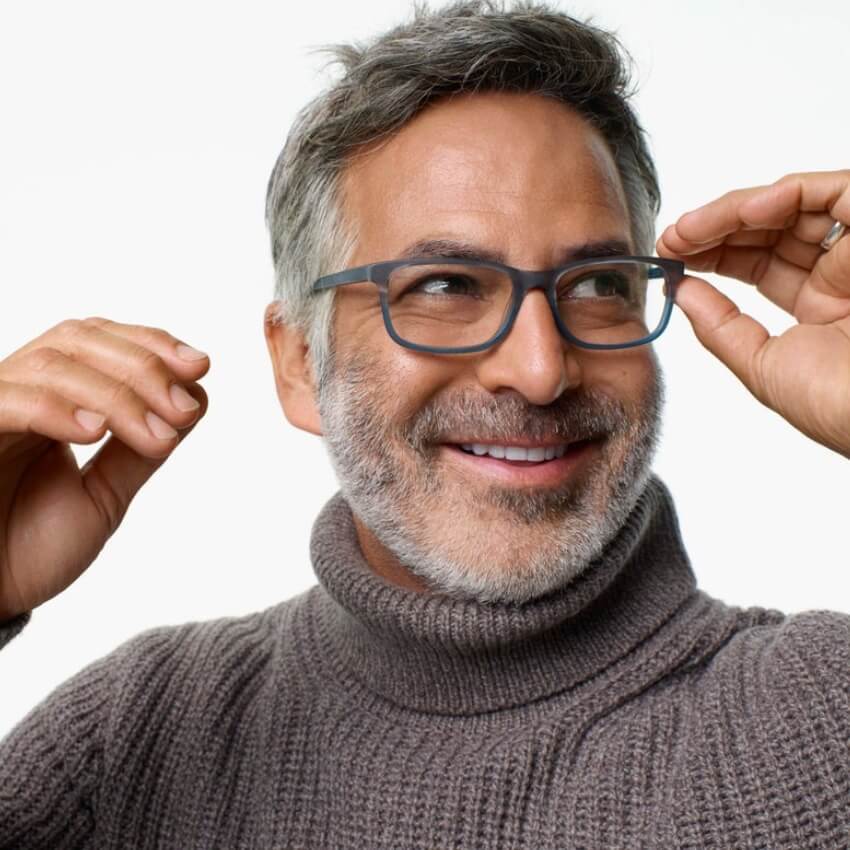 Man wearing dark rectangular glasses and a gray knit turtleneck sweater, adjusting the glasses with both hands.