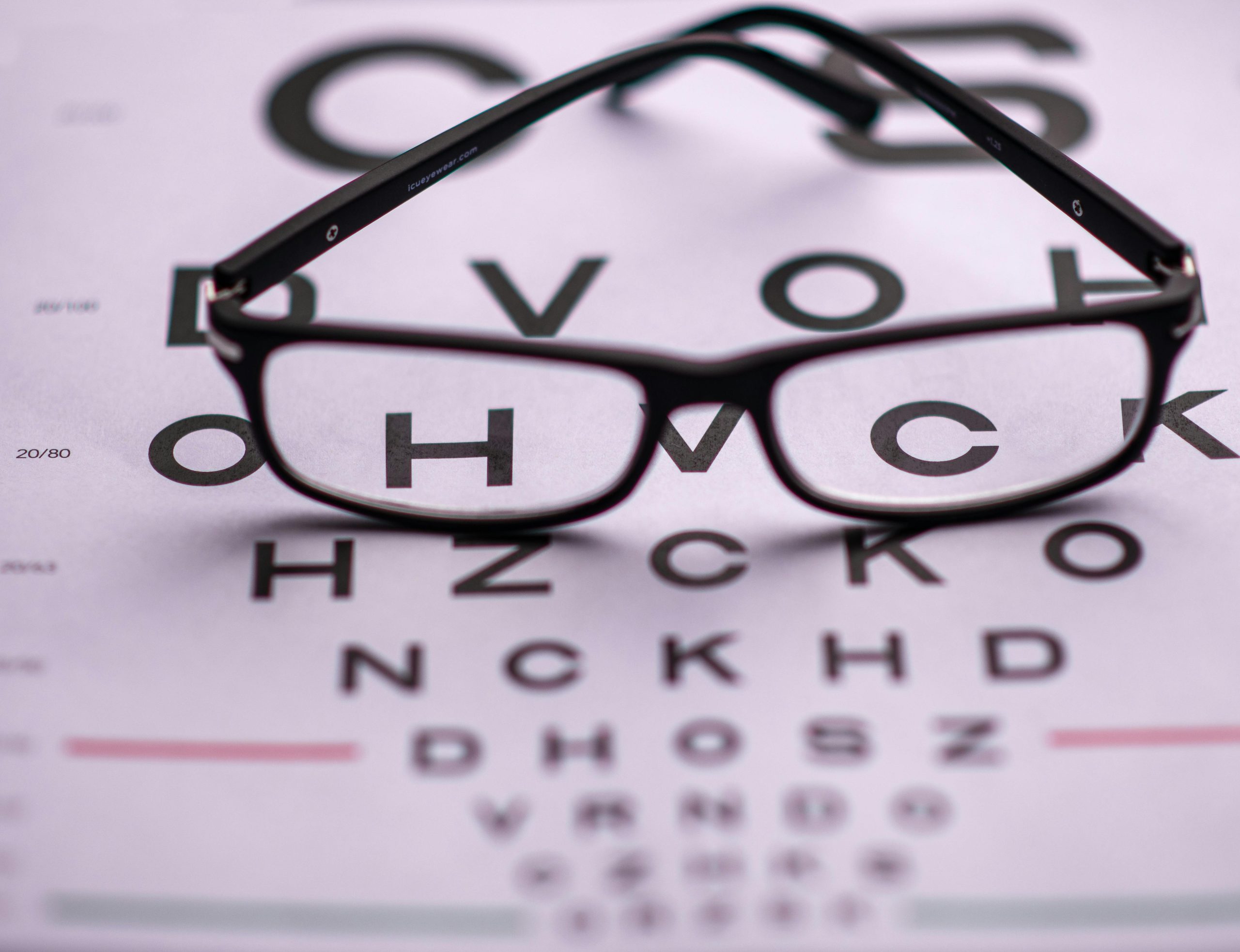 Eyeglasses resting on an eye chart displaying letters: C, D, V, O, H, Z, K, N, C, K, H, D.