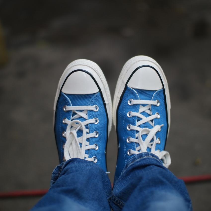 Blue canvas sneakers with white laces and toe caps. Denim jeans are partially visible.