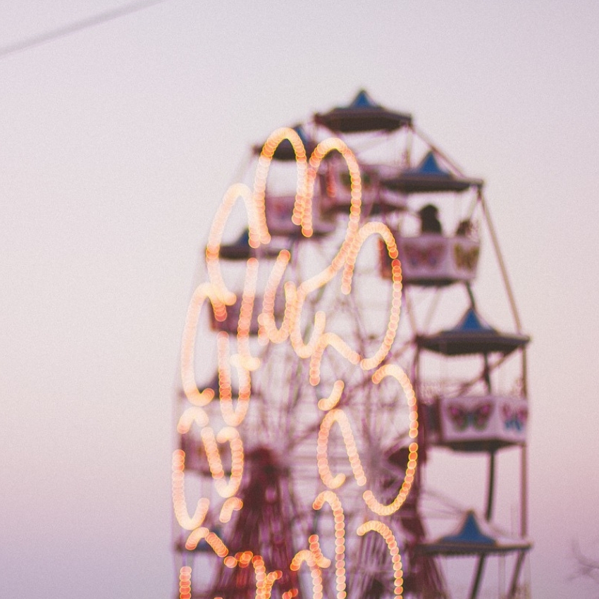 Blurred Ferris wheel with lights glowing at dusk.