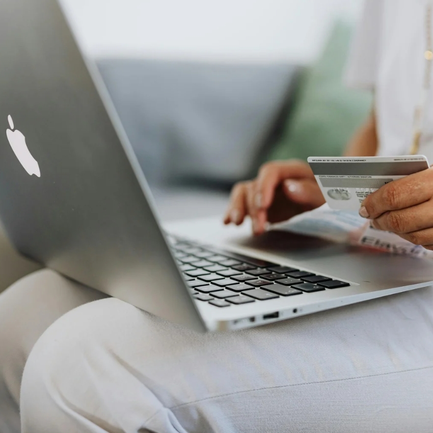Person holding a credit card while using a silver Apple MacBook.