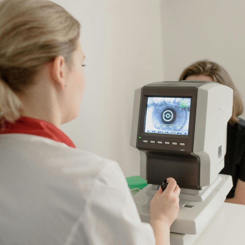 Optometrist using an autorefractor to examine a patient's eye, displaying an eye image on the screen.