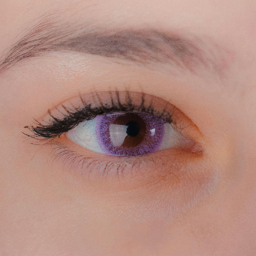 Close-up of a brown eye wearing a purple colored contact lens with detailed iris design.