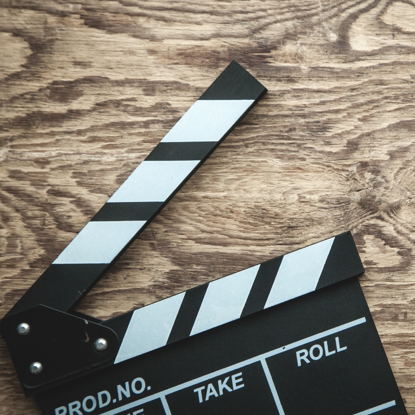 Film clapperboard on wooden surface, text: PROD.NO., DATE, SCENE, TAKE, ROLL.