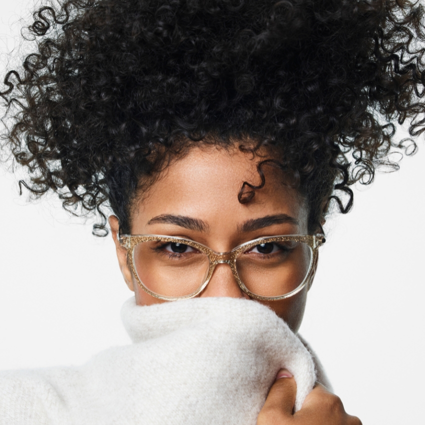 Curly-haired person wearing transparent eyeglasses and a white sweater covering their face.